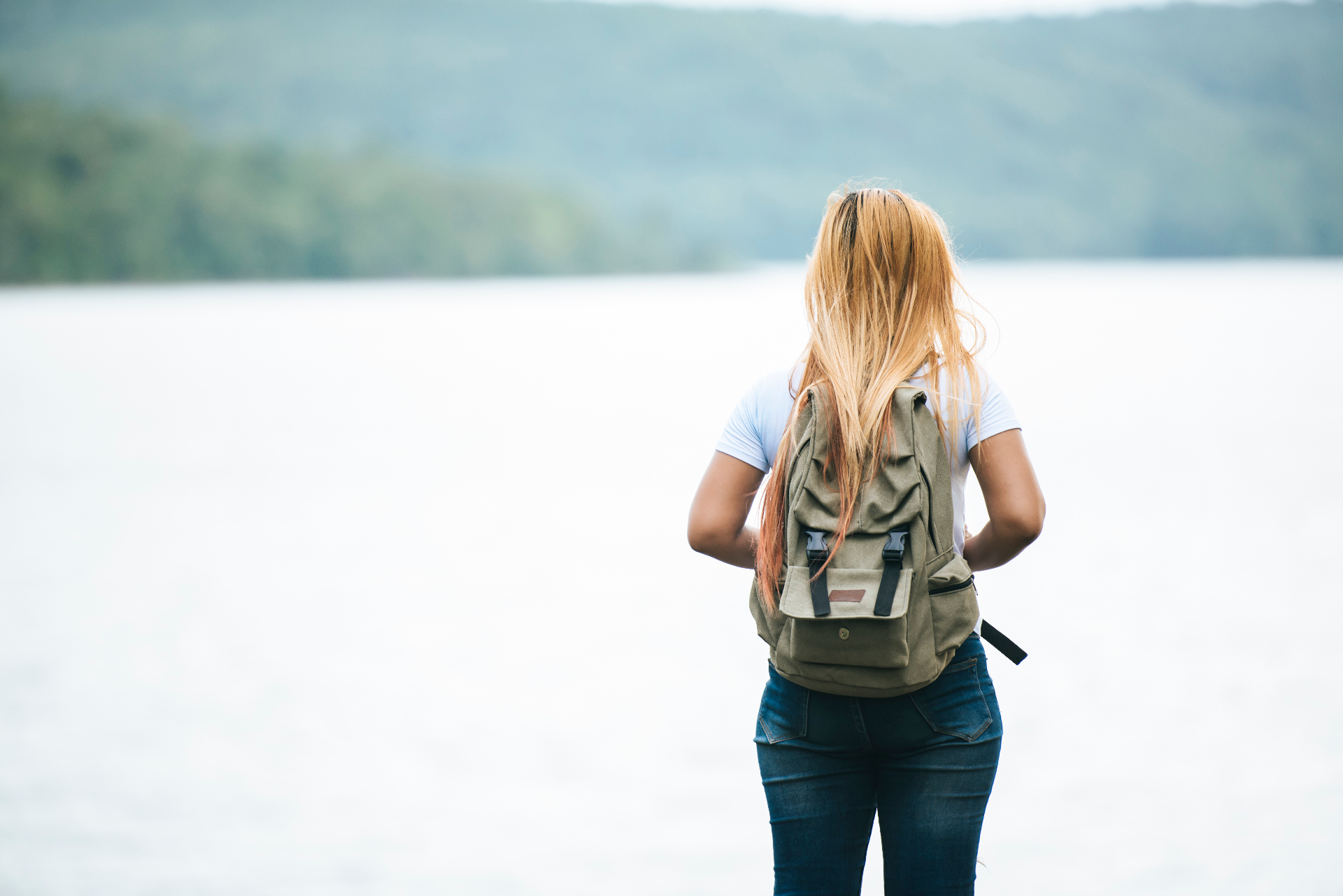 Femme avec les bras levés face à un lac, symbole de liberté et retrouver sa place